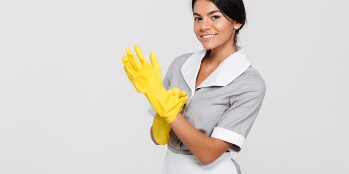 close-up-photo-of-young-smiling-brunette-maid-in-uniform-putting-on-yellow-rubber-gloves-while-standing